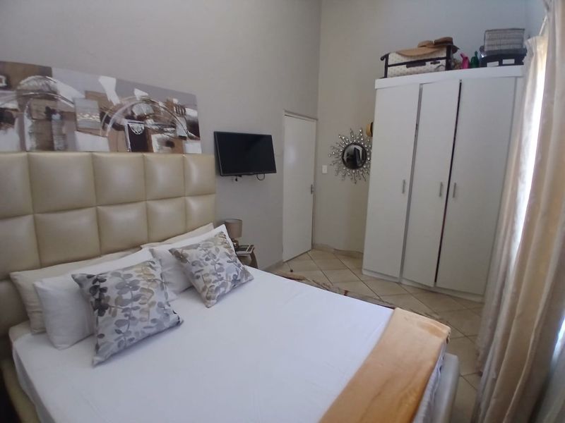 A bedroom featuring tiled flooring, a high ceiling, and a built-in wardrobe, offering a functional and well-lit living space.