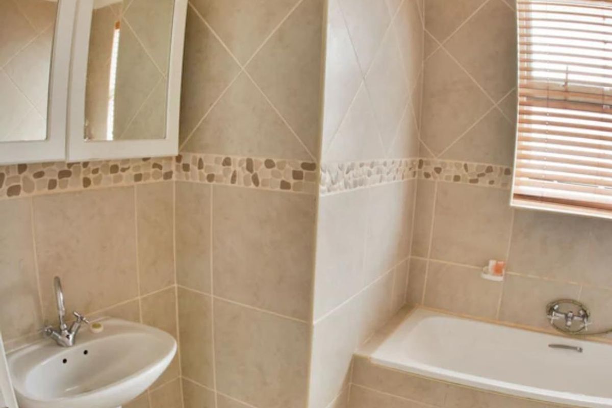 A functional bathroom featuring a pedestal basin, a built-in bathtub with tiled surround, and a mirrored medicine cabinet.