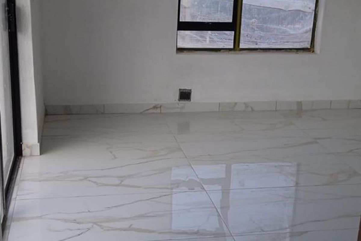 An empty living area featuring polished marble-look porcelain floor tiles, aluminium window frames, and a sliding door, awaiting final finishing touches.