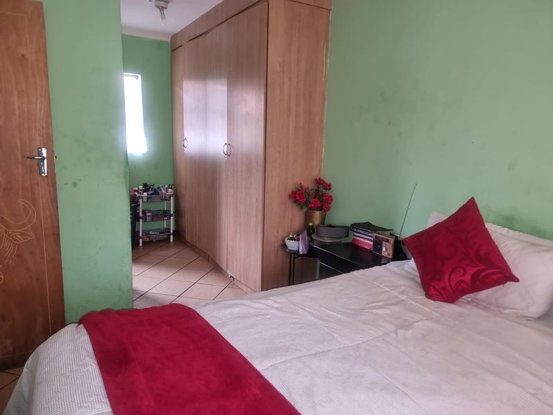 A bedroom featuring built-in wooden cupboards and tiled flooring, requiring cosmetic updates to the wall finishes.