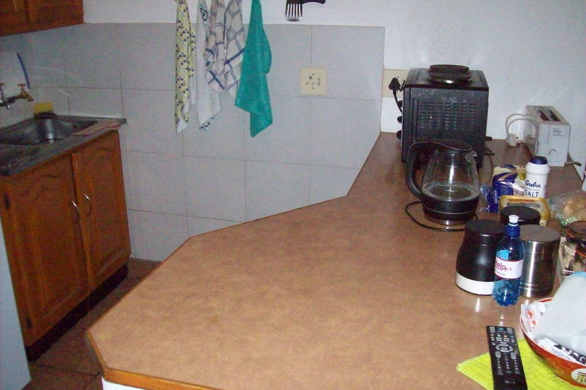 A functional kitchen area featuring wooden cabinetry, a laminate countertop, and a stainless steel sink with tiled backsplash.