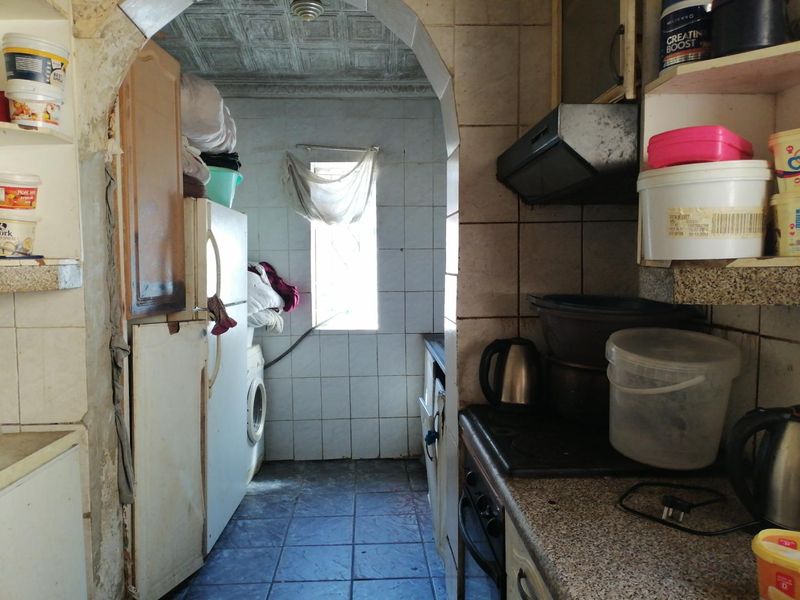 A compact scullery area featuring tiled surfaces, built-in oven, extractor fan, and stone countertops, requiring cosmetic updates and maintenance.