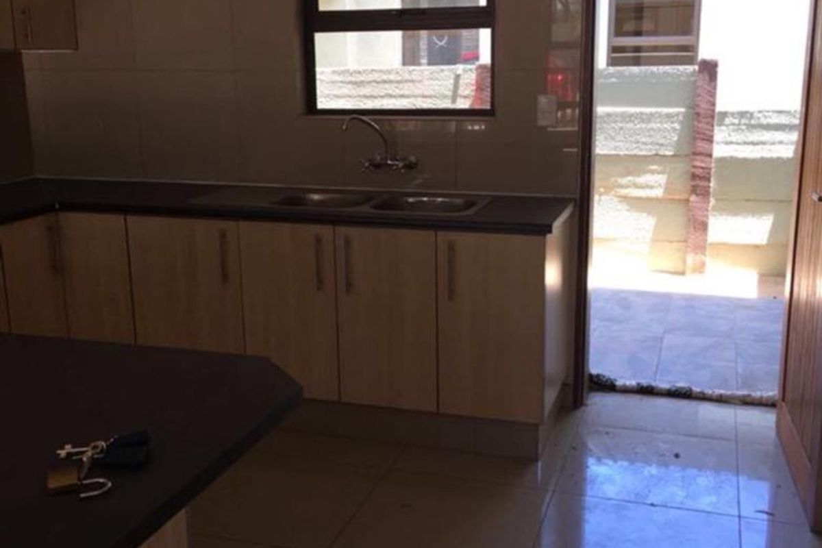 A functional kitchen featuring light wood-look cabinetry, tiled splashbacks, and a double sink, with direct access to an outdoor area.