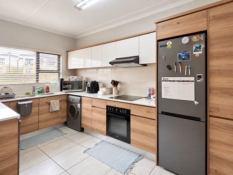 Modern kitchen featuring wood-grain cabinetry, white upper cabinets, integrated appliances, tiled backsplash, and ample counter space with a functional layout.