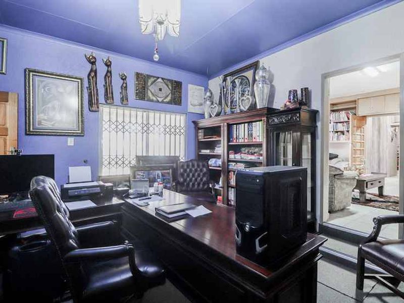 A functional home office space featuring built-in shelving and a security gate on the window, with direct access to an adjacent room.