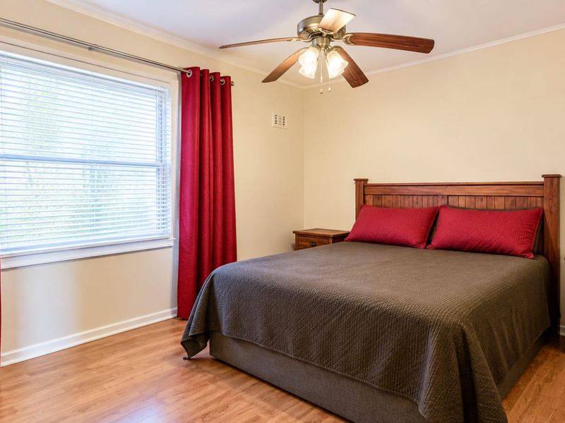 A well-maintained bedroom featuring laminate flooring, a ceiling fan, and large windows with fitted blinds.