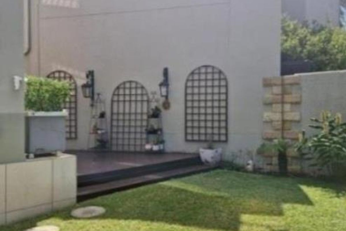 A private rear garden area featuring a raised timber deck, decorative wall trellises, and wall-mounted exterior lighting.