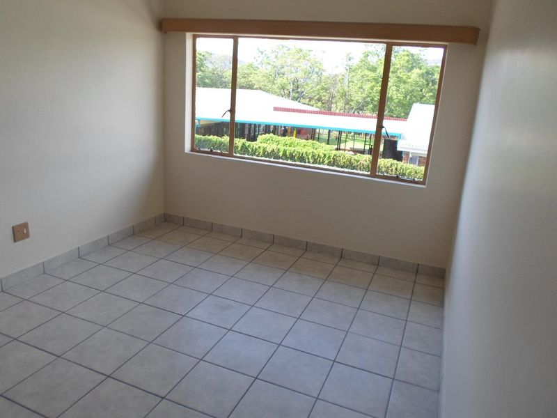 A bright, empty bedroom featuring neutral tiled flooring and a large window with a wooden pelmet, offering a clear view of the surrounding area.