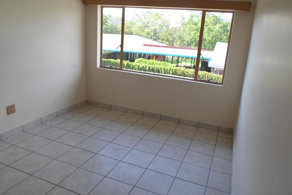 A bright, empty bedroom featuring neutral tiled flooring and a large window with a wooden pelmet, offering a clear view of the surrounding area.