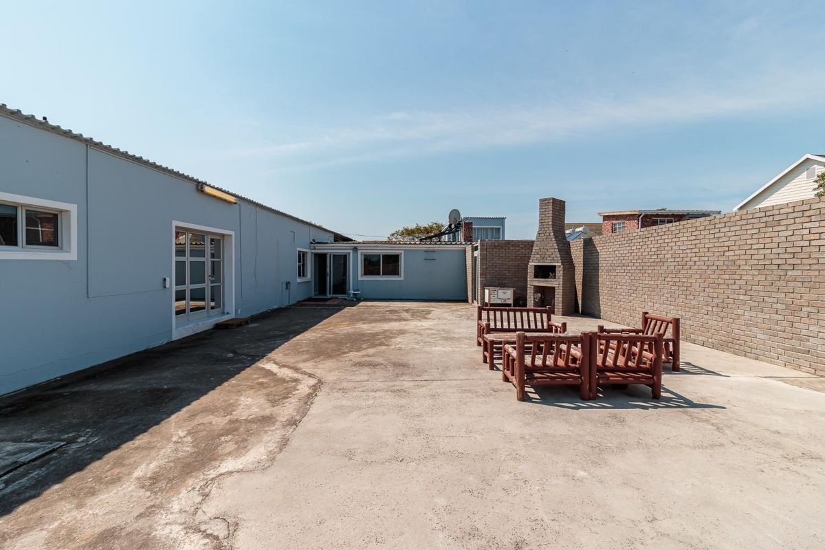 Spacious rear concrete patio featuring a built-in brick braai and enclosed by a brick boundary wall, offering potential for outdoor entertainment.
