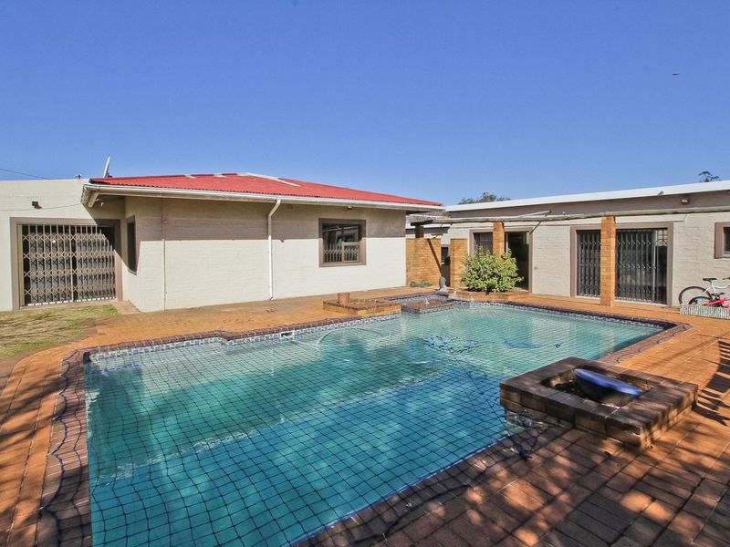 Rear exterior view featuring a swimming pool with a safety net, surrounded by brick paving and accessible via multiple sliding doors.
