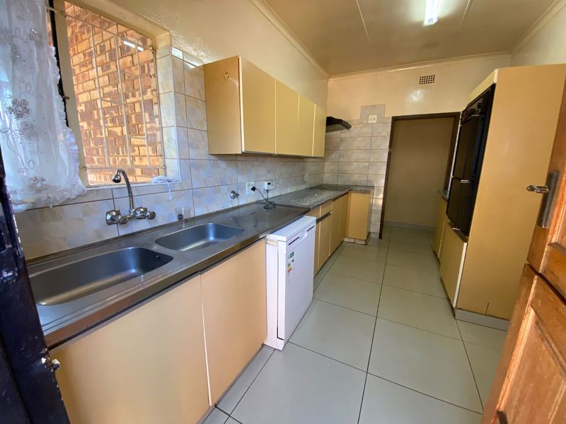 A functional kitchen featuring dated cabinetry, double stainless steel sink, built-in oven, and tiled finishes, offering potential for modern renovation.