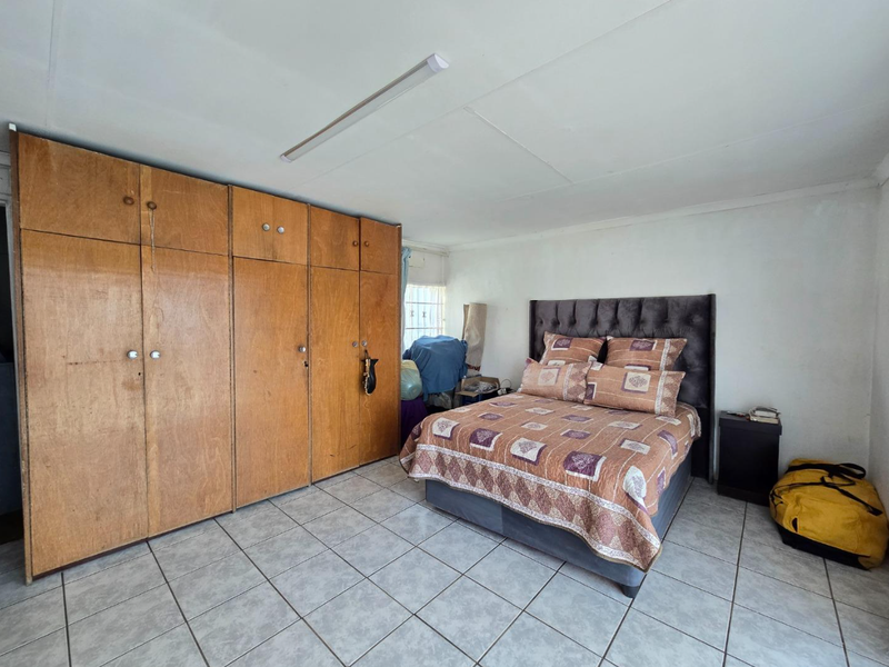 A bedroom featuring built-in wooden cupboards, tiled flooring, and a standard ceiling light fixture.
