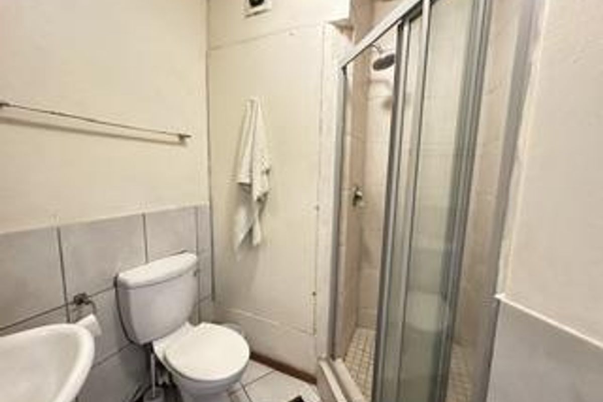 A functional bathroom featuring a shower enclosure, toilet, and wash basin with tiled finishes and an extractor fan.