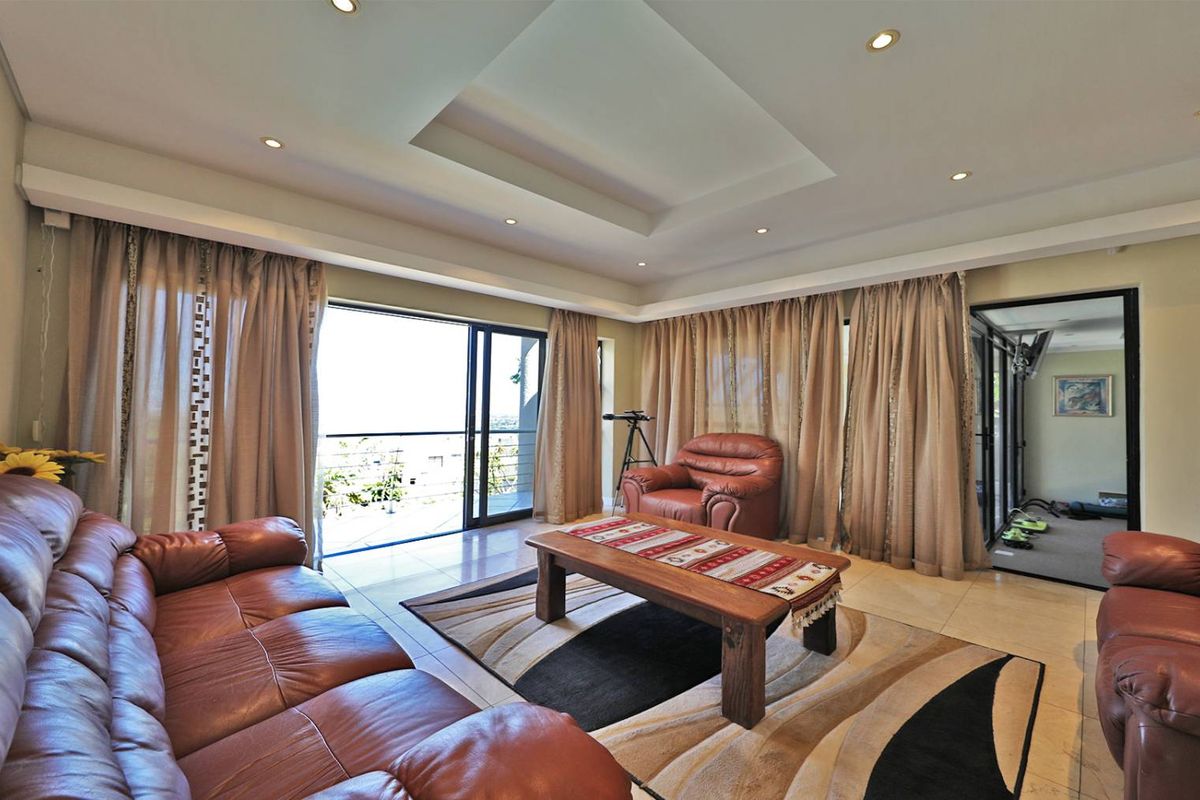 Spacious living room featuring a recessed tray ceiling with integrated downlights, tiled flooring, and large sliding glass doors opening to an outdoor balcony.