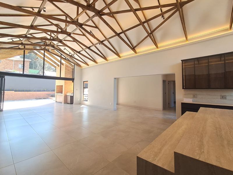 Spacious open-plan living area featuring striking exposed timber trusses, large format tiling, and seamless indoor-outdoor flow through bi-fold doors to the patio.