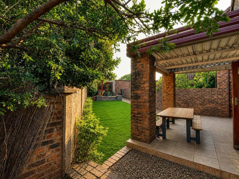 A private rear garden featuring a covered brick patio area, well-maintained lawn, and secure brick boundary walls.