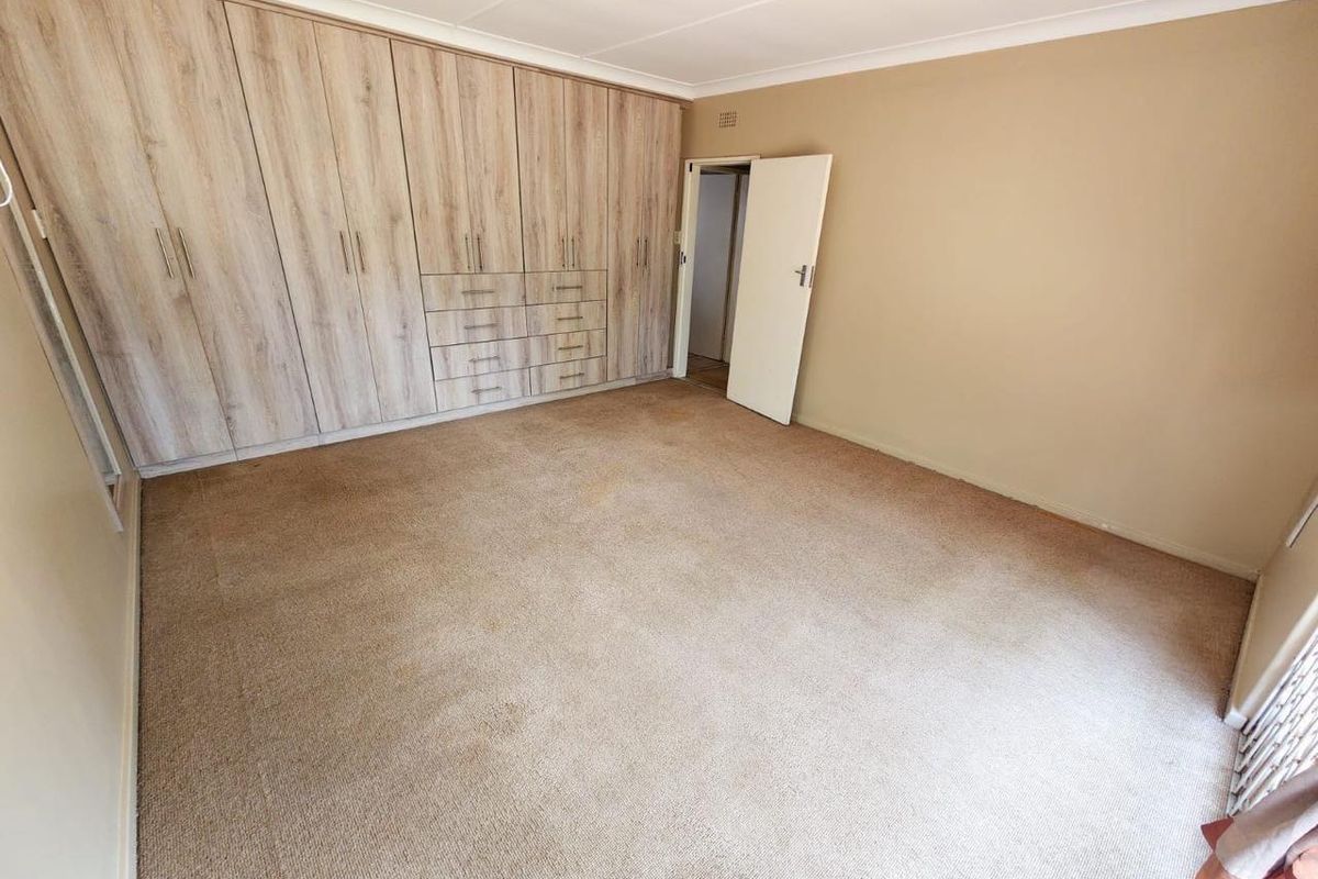 A spacious bedroom featuring extensive built-in wooden cabinetry and neutral wall finishes, providing ample storage space.
