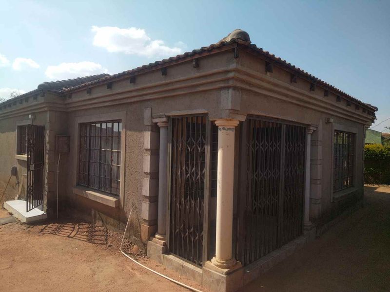 Front exterior view of a single-story house featuring a tiled roof, decorative columns, and security gates installed on windows and doors.