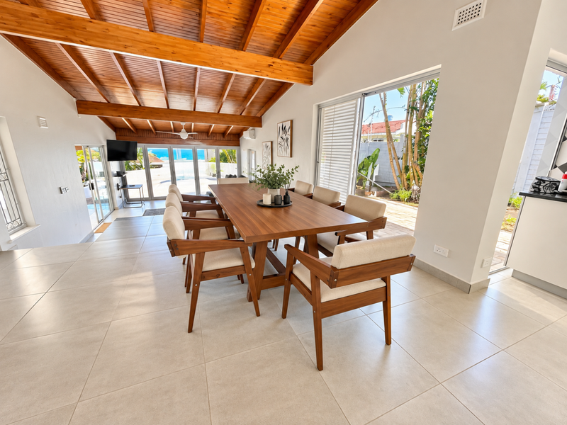 Spacious open-plan dining area featuring a vaulted timber beam ceiling, large format floor tiles, and seamless access to the outdoor patio through sliding glass doors.