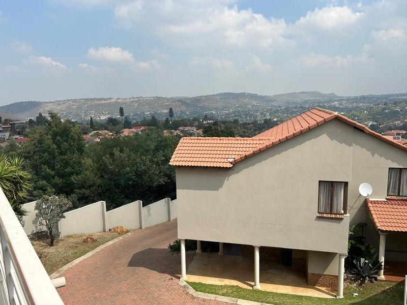 Elevated view of the townhouse rear exterior featuring a paved driveway, terracotta tiled roof, and scenic hillside landscape.