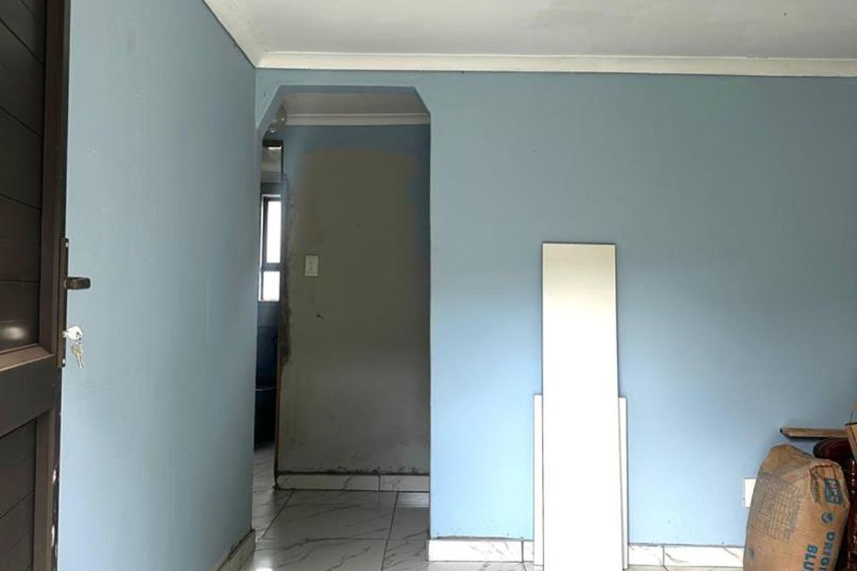 An interior view of a room featuring marble-look floor tiles and blue painted walls, currently undergoing renovation with unfinished wall sections.