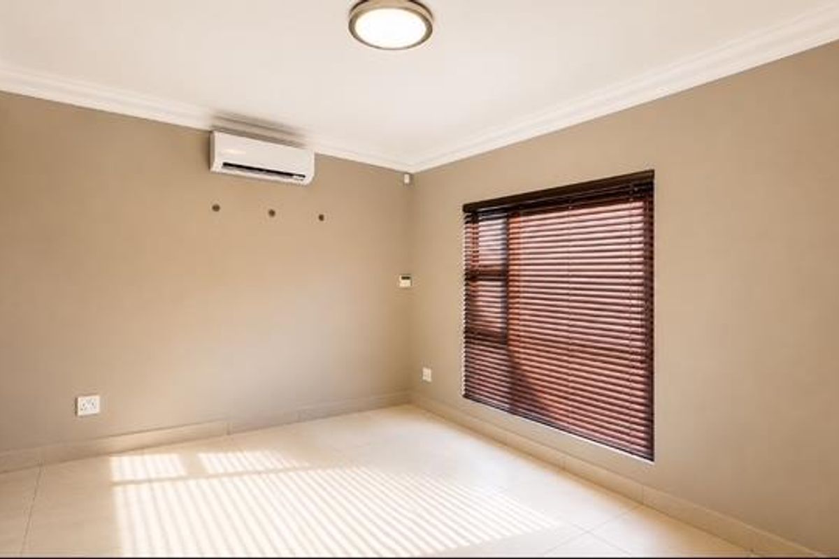 A bright, empty bedroom featuring tiled flooring, built-in cupboards, an air conditioning unit, and venetian blinds.