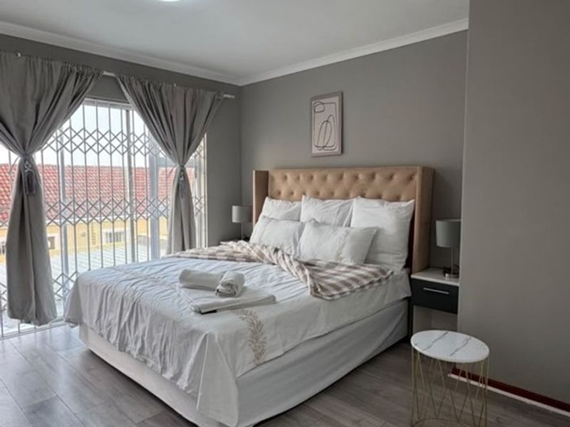 A well-maintained bedroom featuring modern laminate flooring, neutral wall tones, and a sliding door with integrated security gate providing natural light.