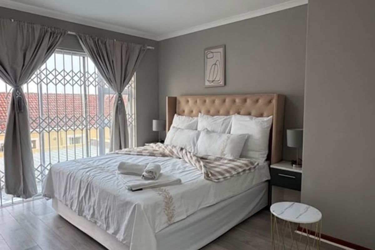 A well-maintained bedroom featuring modern laminate flooring, neutral wall tones, and a sliding door with integrated security gate providing natural light.