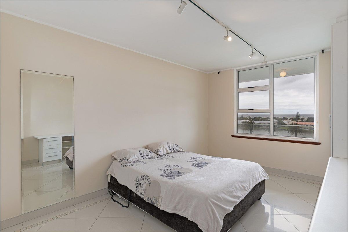 A bright bedroom featuring tiled flooring, track lighting, and a large window with scenic views, complemented by a full-length wall mirror.
