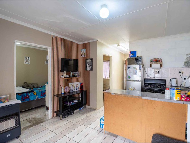 Open-plan living and kitchen area featuring tiled flooring, a breakfast counter, and functional kitchen cabinetry with a gas stove.