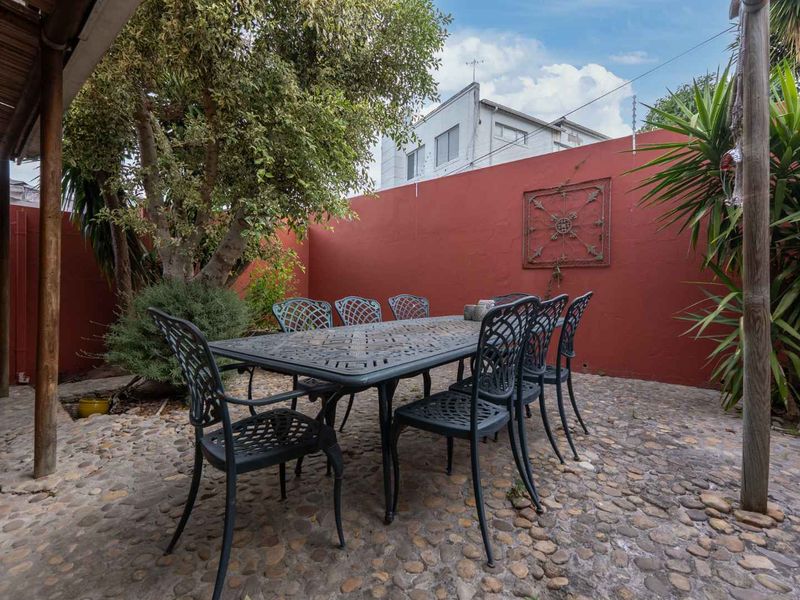 A private outdoor patio area featuring pebble flooring, a timber pergola structure, and a high boundary wall, suitable for outdoor dining and relaxation.