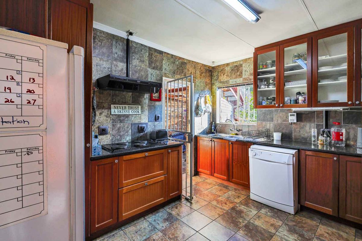 A functional kitchen featuring dark wood cabinetry, granite countertops, tiled splashbacks, and a built-in hob with an extractor fan.
