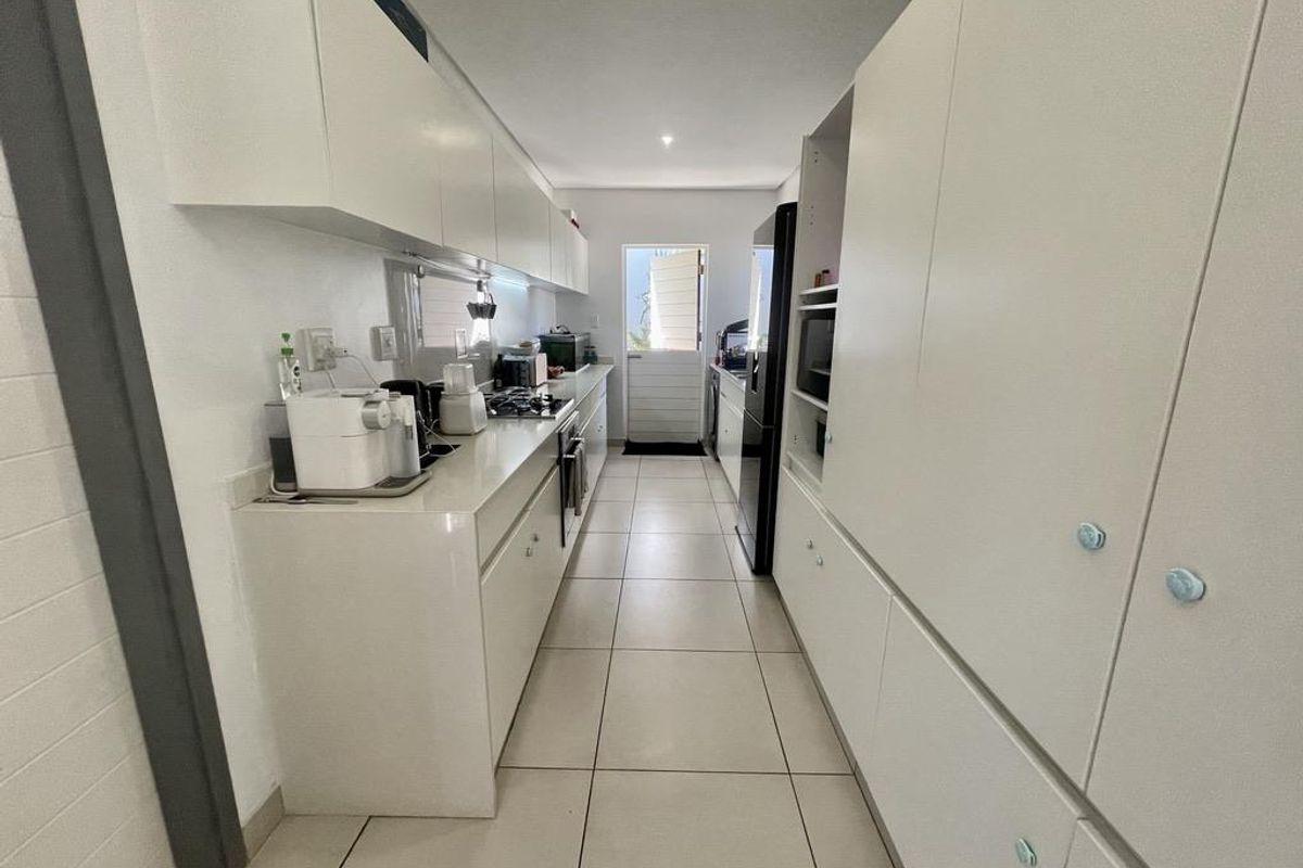 A galley-style kitchen featuring white cabinetry, stone countertops, a built-in gas hob, and tiled flooring, leading to an exterior door.