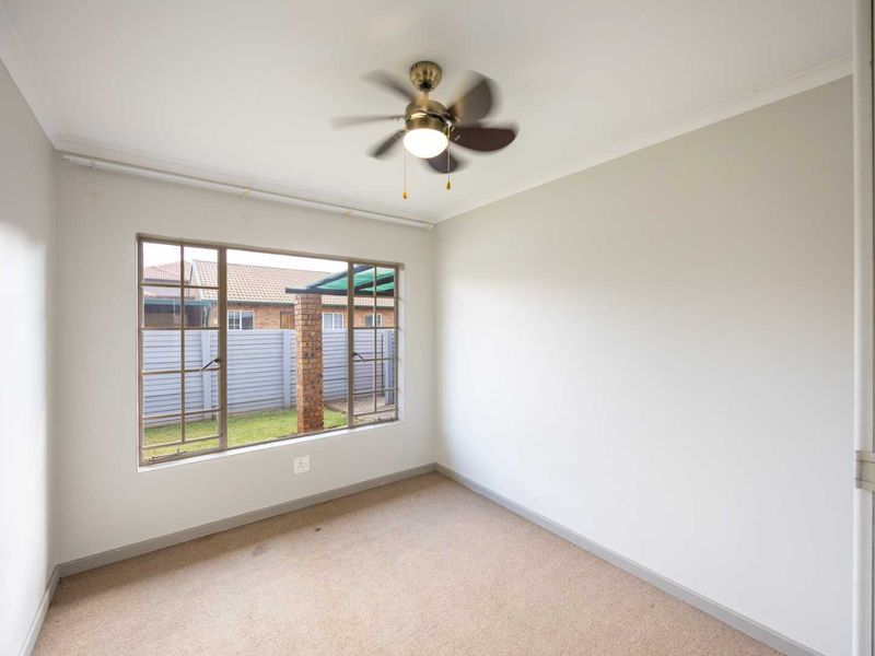 A vacant bedroom featuring neutral walls, carpet flooring, a ceiling fan, and a large window overlooking the rear garden area.