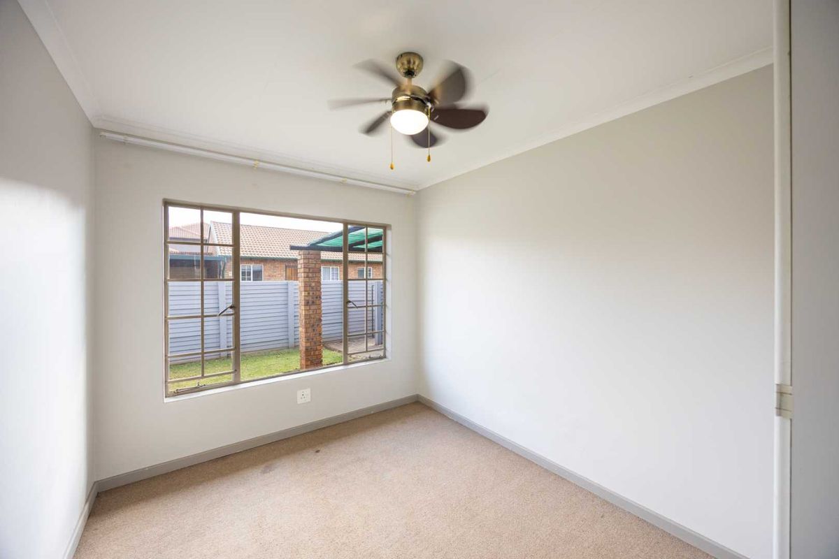A vacant bedroom featuring neutral walls, carpet flooring, a ceiling fan, and a large window overlooking the rear garden area.