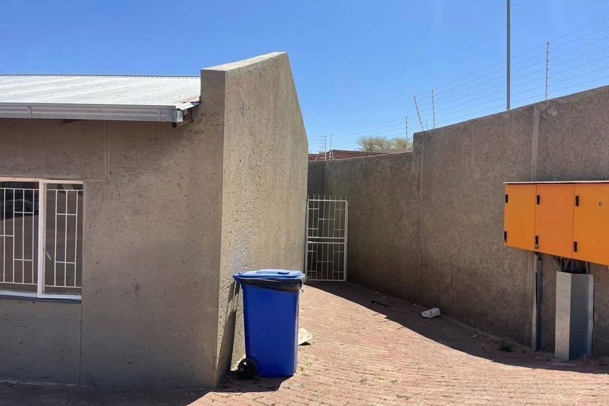 A view of the exterior rear area featuring paved ground, perimeter boundary walls with electric fencing, and a metal security gate.
