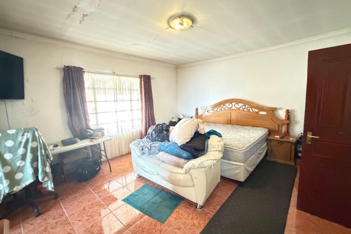 A spacious bedroom featuring tiled flooring and a large window, requiring cosmetic updates to the ceiling and finishes to restore its appeal.