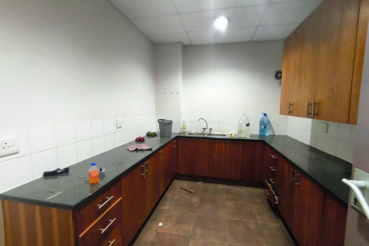A functional industrial kitchen area featuring dark wood-look cabinetry, granite countertops, a double sink, and tiled flooring with a drop ceiling.