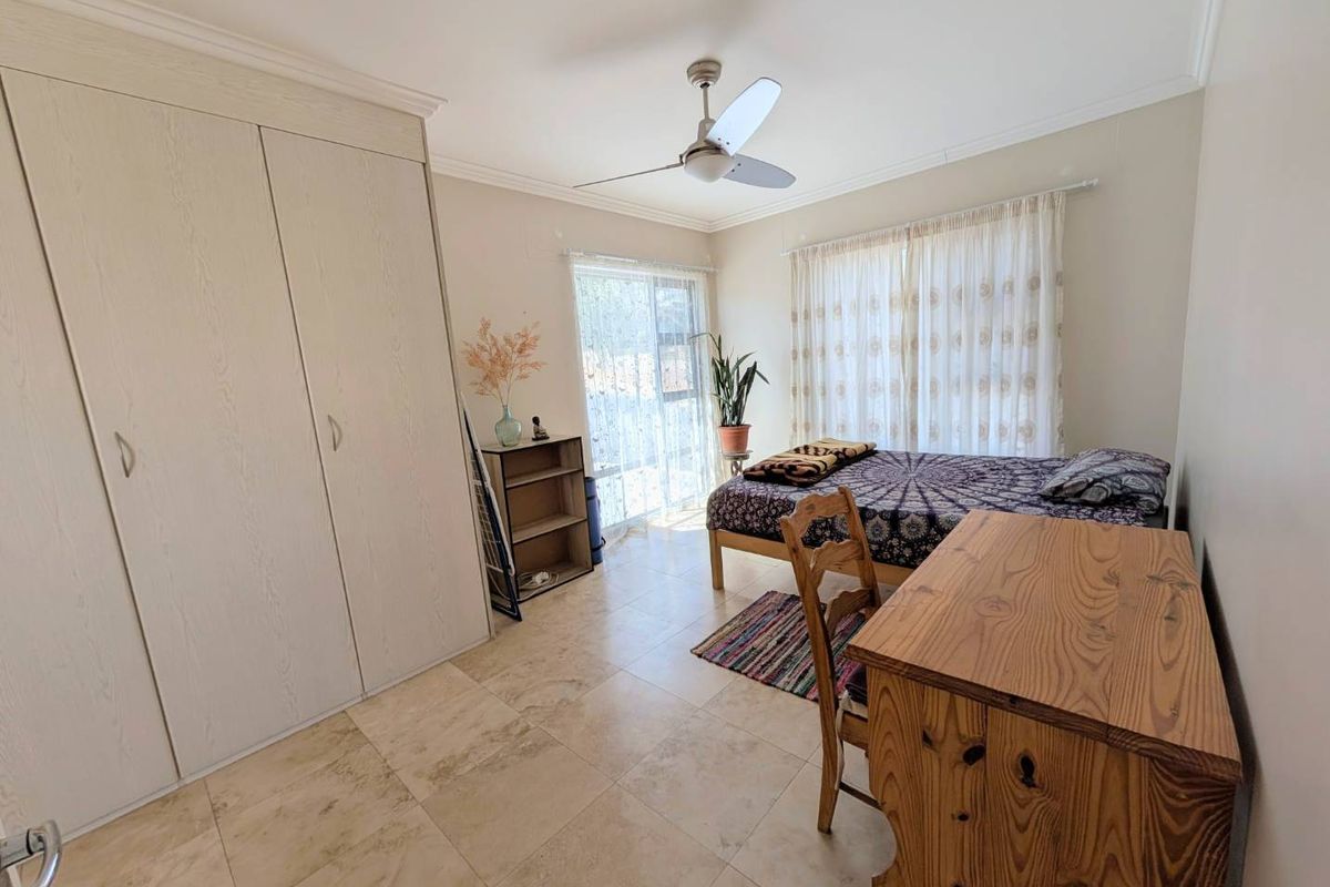 A bedroom featuring tiled flooring, built-in cupboards, a ceiling fan, and a sliding glass door providing natural light.
