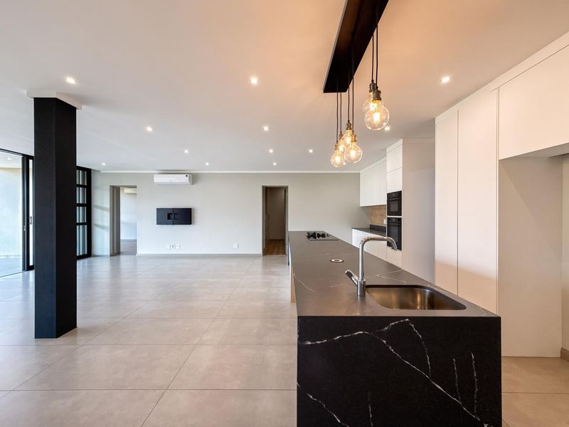 Spacious open-plan living and kitchen area featuring a modern kitchen island with stone countertops, built-in appliances, tiled flooring, and large sliding doors.