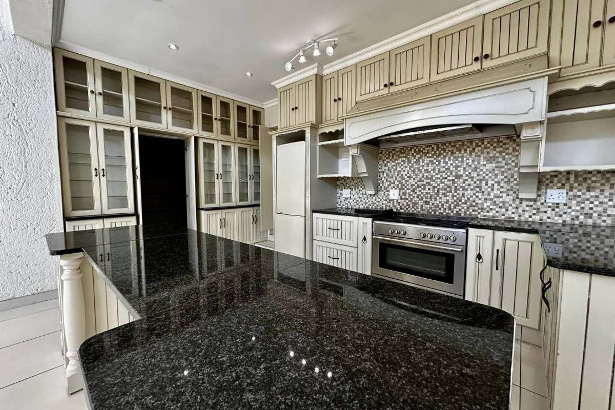 Spacious kitchen featuring extensive built-in cabinetry, a large granite-topped island, mosaic tile backsplash, and integrated oven with extractor fan.