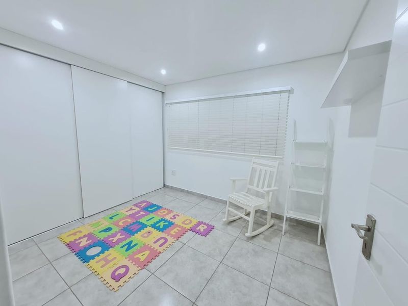 A bright, neutral bedroom featuring tiled flooring, recessed downlights, venetian blinds, and a large built-in sliding door wardrobe.