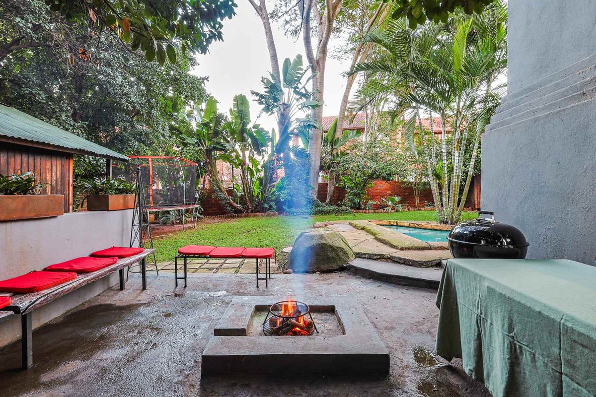 A private rear garden featuring a paved patio with a built-in fire pit, a swimming pool, and established trees and landscaping.