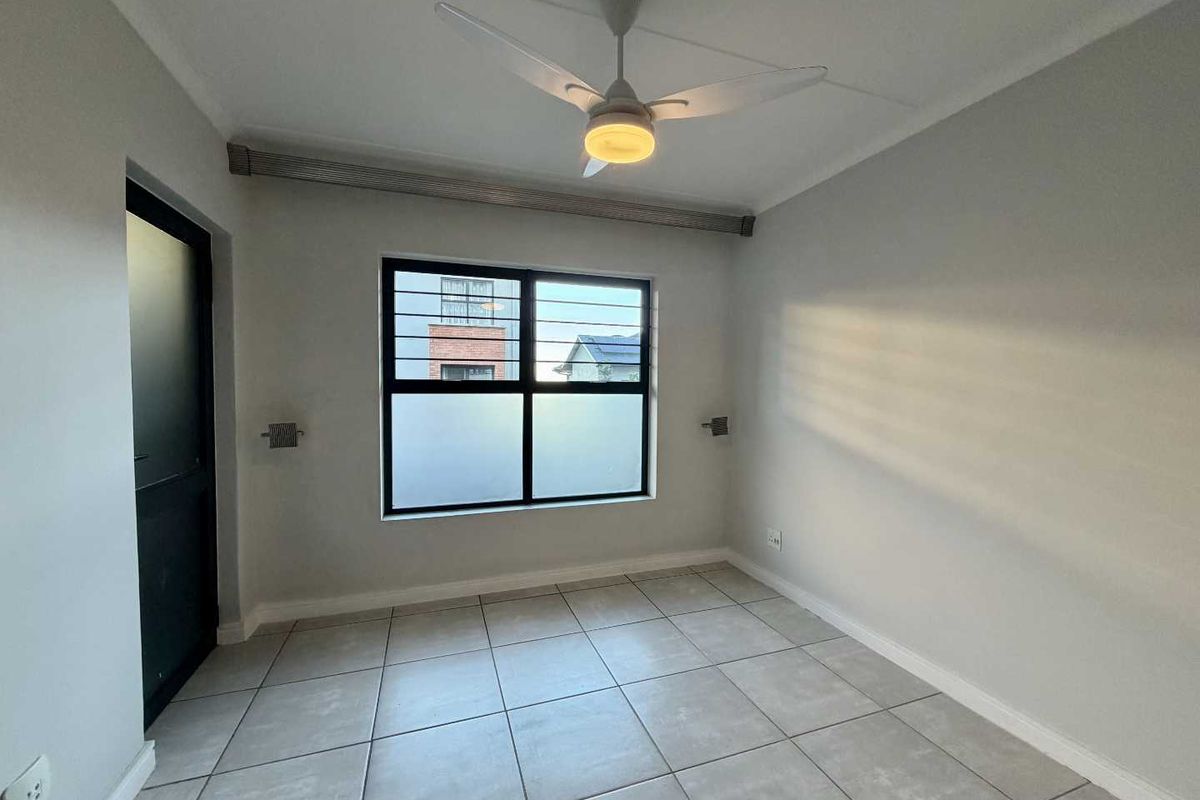 A clean, empty bedroom featuring neutral tiled flooring, a ceiling fan, and a window fitted with security bars.