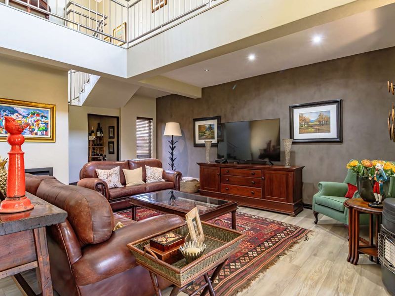 Spacious double-volume living room featuring a mezzanine level, modern recessed lighting, and a dark feature wall, creating an open and airy atmosphere.