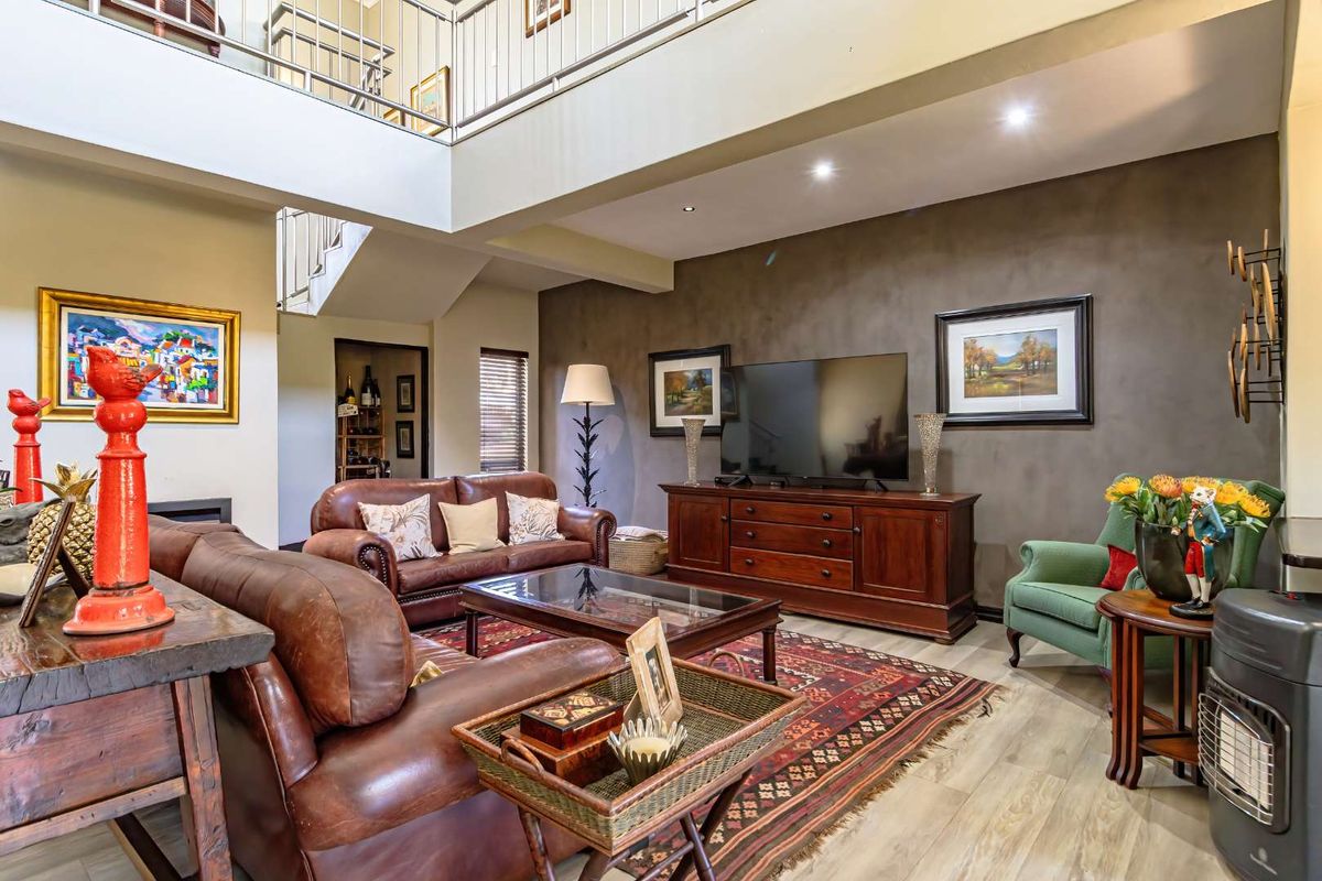 Spacious double-volume living room featuring a mezzanine level, modern recessed lighting, and a dark feature wall, creating an open and airy atmosphere.