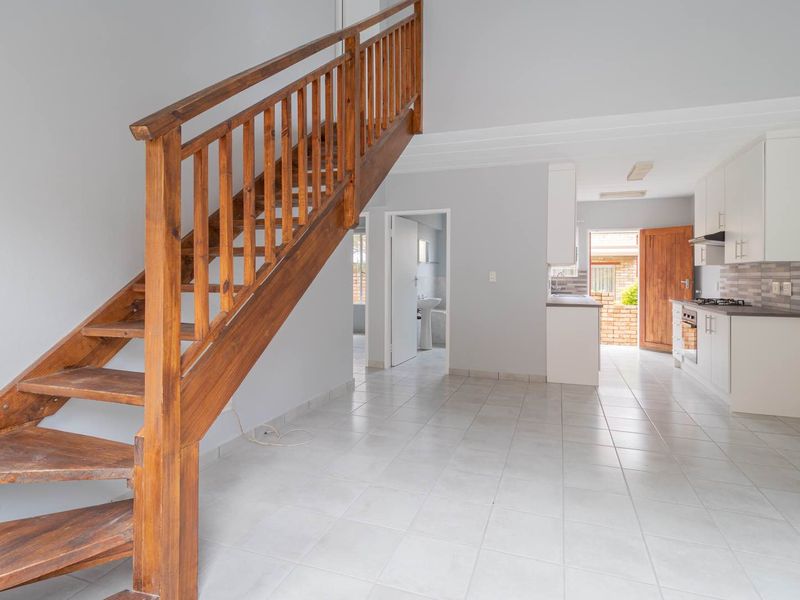 Open-plan living area featuring a wooden staircase, tiled flooring, and a functional kitchen with built-in appliances and direct access to the rear exterior.