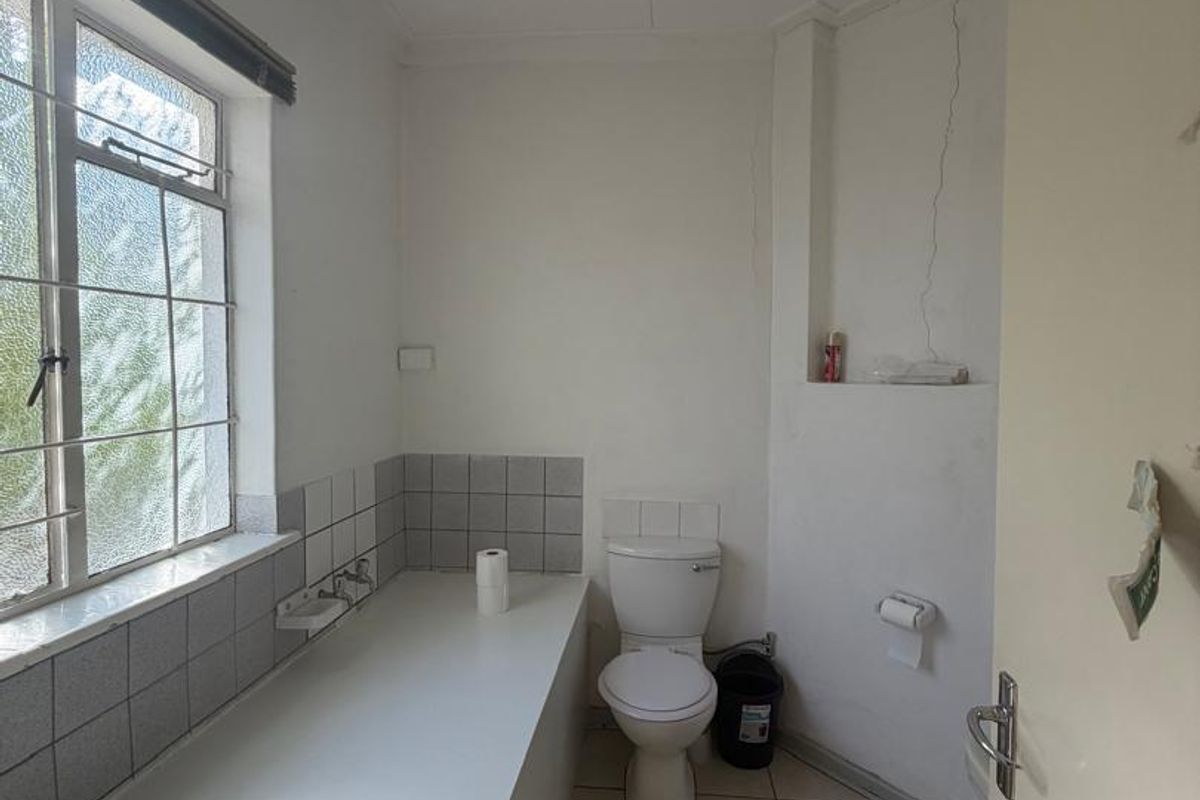 A functional bathroom featuring a built-in bathtub, toilet, and tiled flooring. The space requires cosmetic updates and repairs to address visible wall cracking.