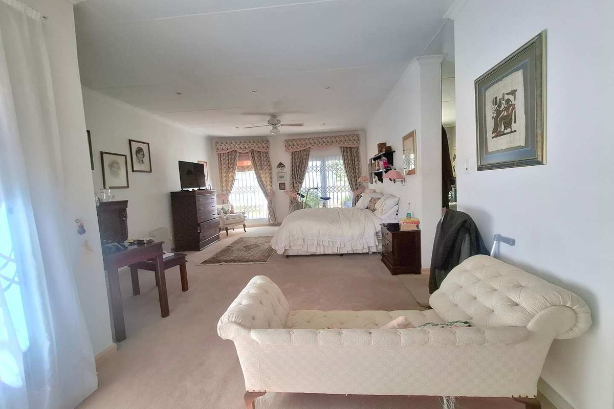 Spacious bedroom featuring neutral carpeting, a ceiling fan, and large windows with security gates, offering a comfortable and well-lit living space.